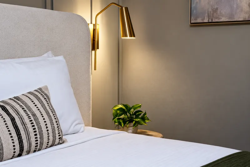 Brass wall sconce over an upholstered headboard with striped pillow