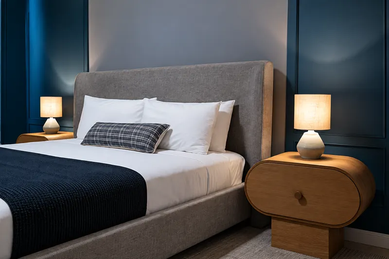 Bed with gray headboard, rounded wood nightstands and table lamps