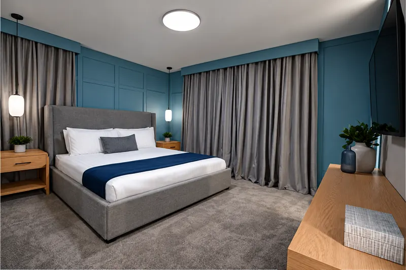 Blue bedroom with floor-to-ceiling gray drapes and wood dresser